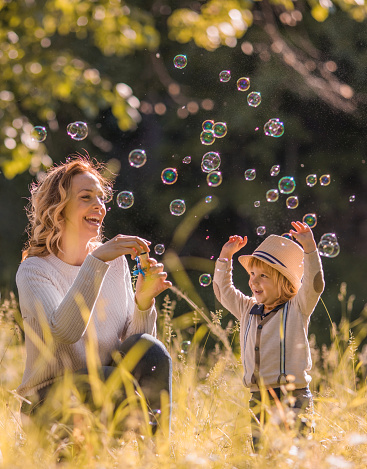 Happy mother having fun with her little boy while blowing bubbles in grass.