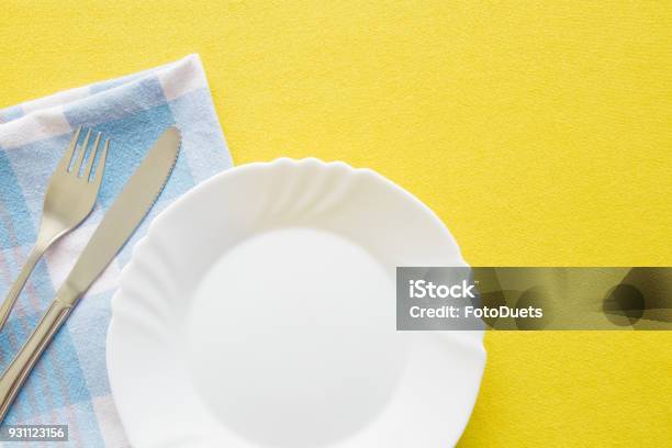 Clean Empty White Plate Fork And Knife With Yellow Tablecloth And Blue Towel On A Table Cutlery Concept Flat Lay Top View Free Space For Text Or A Logo Stock Photo - Download Image Now