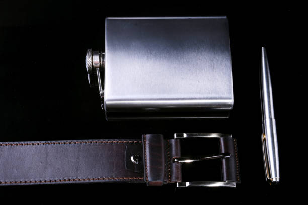 istock Stainless hip flask, lighter, pen and luxury belt isolated on mirror black background. 931123252