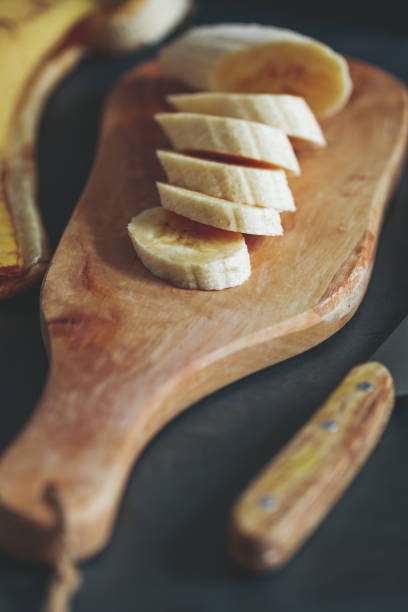 Chopped banana on a rustic wooden board over black table.