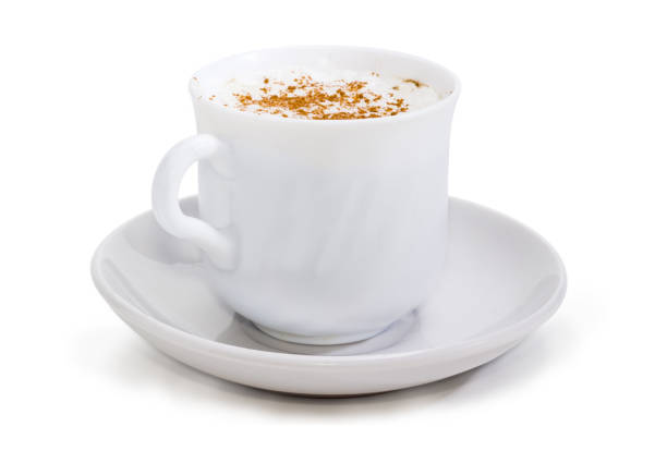 Coffee with foamed cream sprinkled with cinnamon powder in the white cup on the saucer closeup at selective focus on a white background