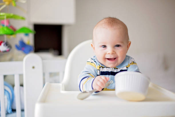 schattige kleine baby jongen, gepureerde groenten eten voor de lunch, moeder hem voeden - jongen peuter eten stockfoto's en -beelden