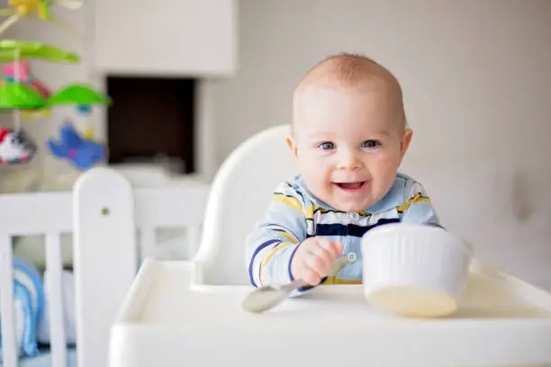 Cute little baby boy, eating mashed vegetables for lunch, mom feeding him, sweet toddler boy, smiling