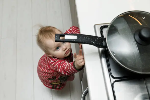 Photo of child safety at home concept - toddler reaching for pan on the stove in kitchen