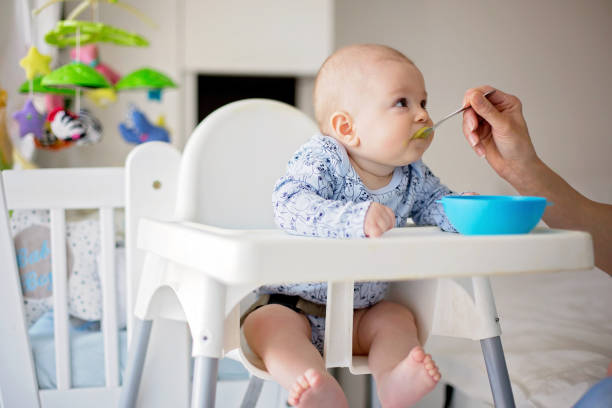 istock Cute little baby boy, eating mashed vegetables for lunch, mom feeding him 931131508