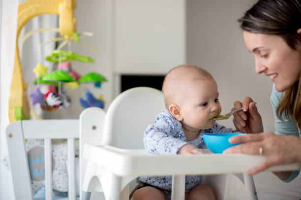 istock Cute little baby boy, eating mashed vegetables for lunch, mom feeding him 931131624