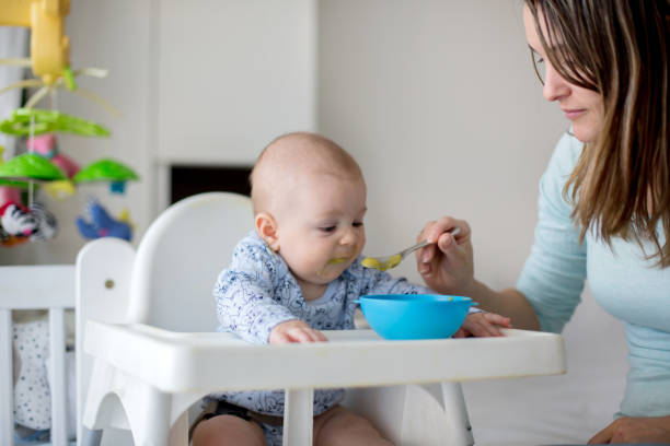 istock Cute little baby boy, eating mashed vegetables for lunch, mom feeding him 931131670