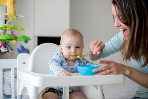istock Cute little baby boy, eating mashed vegetables for lunch, mom feeding him 931131710