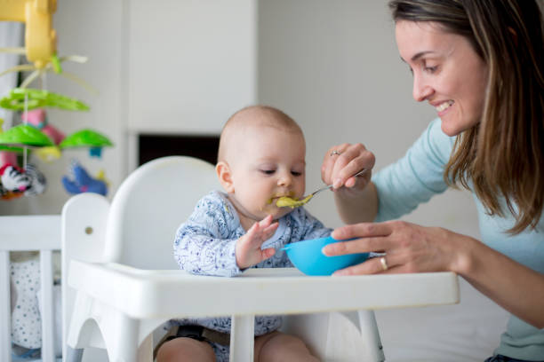 istock Cute little baby boy, eating mashed vegetables for lunch, mom feeding him 931133748