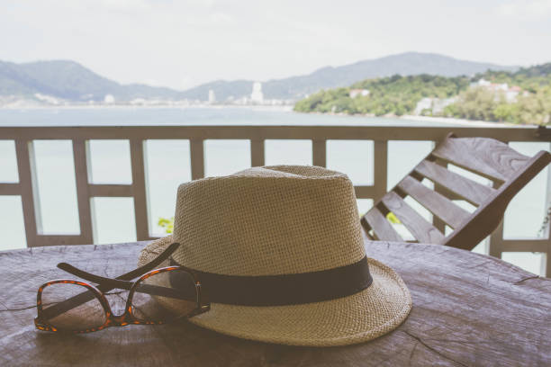 woven vintage hat and sunglasses on wood table with background of the beach