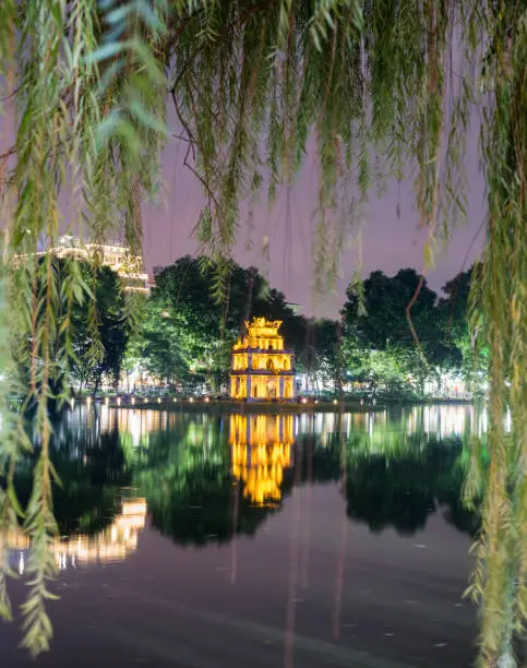 View of Turtle tower through weeping willow tree in Hoan Kiem lake, Hanoi, Vietnam