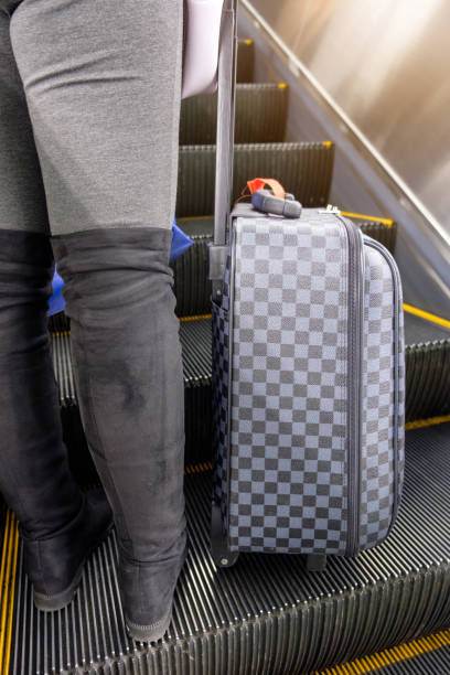istock Young woman wear boot lower half with chess luggage standing on escalator 931155922