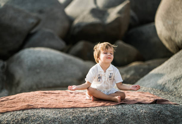 Little boy sitting on a rock at the beach and doing meditation exercises in Lotus position. Cute small boy exercising Yoga in Lotus position on a rock. koh tao thailand stock pictures, royalty-free photos & images