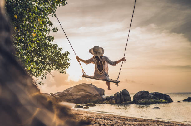 Rear view of a woman swinging during summer vacation on a beach. Back view of carefree woman swinging on a beach at sunset. koh tao thailand stock pictures, royalty-free photos & images