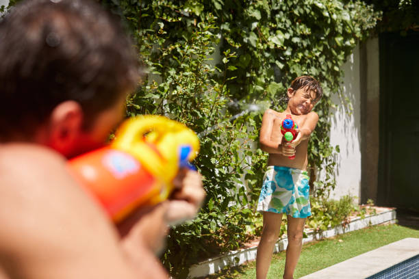 Shot of a father and son playing with squirt guns at the swimming pool at home