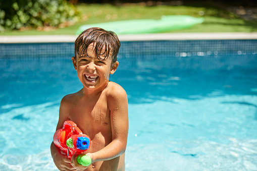 Shot of a little boy holding a water gun in the swimming pool at home