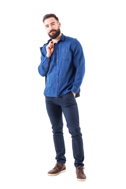 heureux homme souriant décontracté dans une chemise en denim bleu portant la veste sur l’épaule, regardant la caméra - caméra à lépaule photos et images de collection