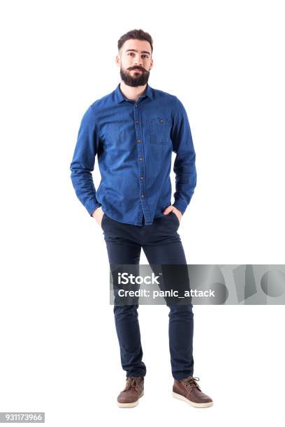 Foto de Jovem Relaxado Usando Camisa Azul Jeans Com As Mãos Nos Bolsos Olhando Para A Câmera e mais fotos de stock de Homens