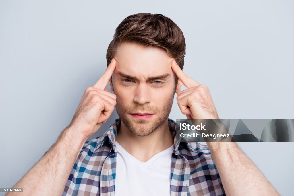 Close up portrait of attractive, concentrated  guy thinking about something, holding fingers on temple, trying to find a solution, ideas, having bad memory, headache, standing over grey background Memories Stock Photo