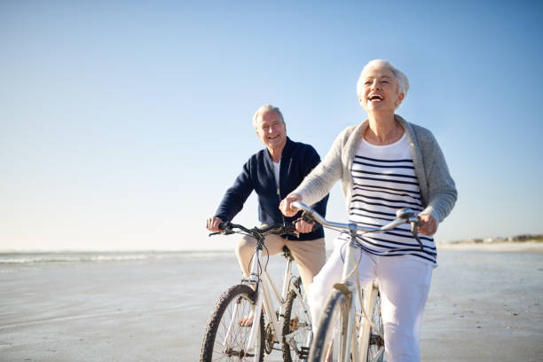 ils apprécient vraiment une balade sur la plage - senior couple cycling beach bicycle photos et images de collection