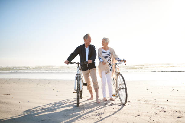 lorsque vous la retraite, chaque jour est un jour férié - senior couple cycling beach bicycle photos et images de collection