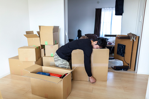 A tired Japanese man is sleeping on a cardboard box in his new house.