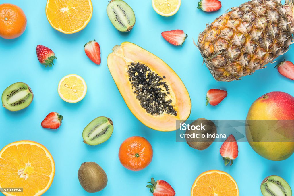 Vielzahl von verschiedenen tropischen saisonale Sommerfrüchten. Papaya Mango Mandarinen Zitrusfrüchte Orangen Ananas Zitronen Erdbeeren Kiwi auf blauem Hintergrund. Gesunden Lebensstil Ernährung Vitamine. Flache Lay - Lizenzfrei Obst Stock-Foto