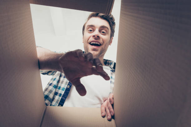 hipster mercancías cabeza camisa a cuadros mano brazo cámara casa piensa mover objetos personas concepto. chico emocionado alegre regocijo tomando su nueva adquisición de la parte inferior de la caja con la palma de - adicto a las compras fotografías e imágenes de stock