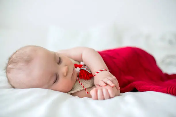 Photo of Cute baby toddler boy, playing with white and red bracelets