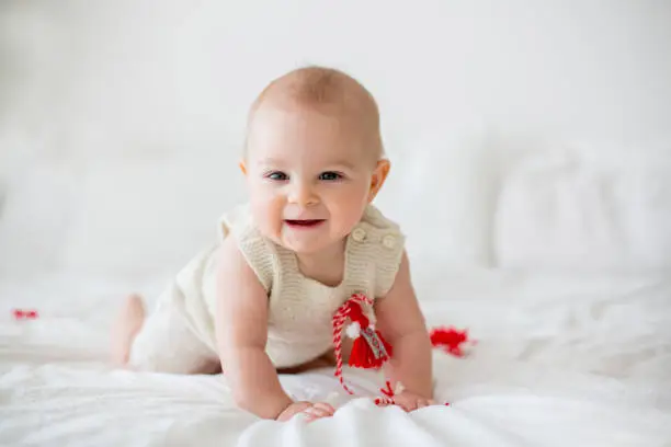 Photo of Cute baby toddler boy, playing with white and red bracelets