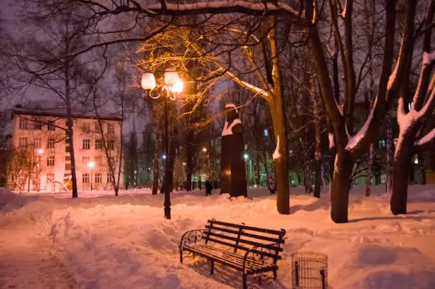 Deep snow in the town park with benches, trees and street lights. Winter night photo park with snowdrifts