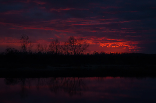 a view of some tree silhouettes at sunset over a lake during autumn