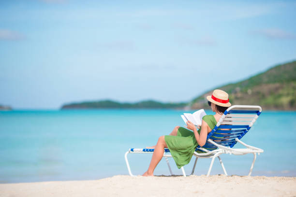 istock Young woman reading book on chaise-lounge on the beach 931227246