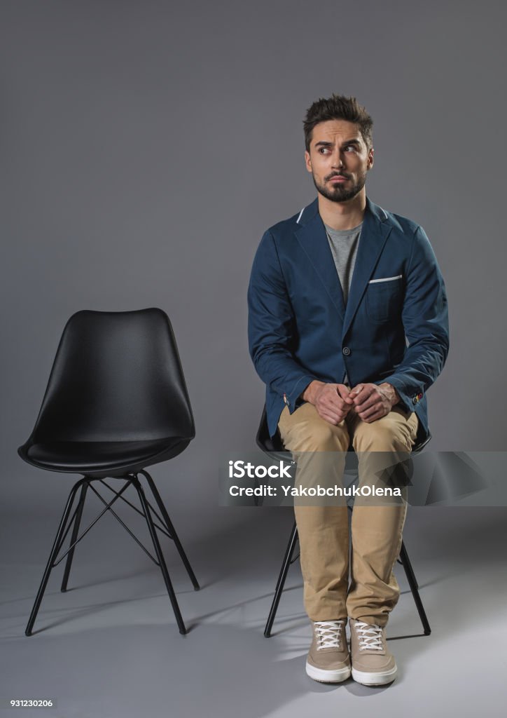 Young excited man sitting on the chair Full length portrait of nervous male is open-eyed. He is waiting for his turn on chair. Copy space in left side Sitting Stock Photo