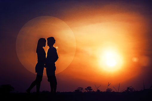 The silhouette of romantic couple lovers hugging and kissing at sunset. The fantasy and love concept.