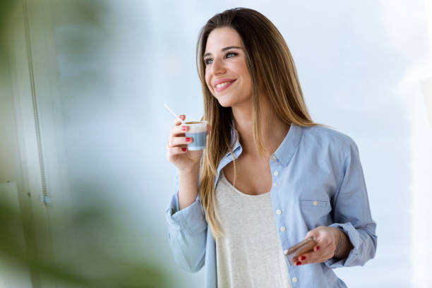 istock Beautiful young woman drinking coffee while using her mobile phone at home. 931239306