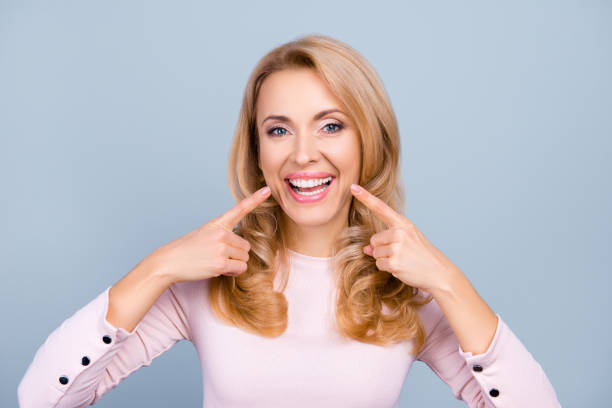 pretty, modern woman in casual outfit pointing with two forefingers to her beaming healthy smile over grey background - hairstyle crest imagens e fotografias de stock