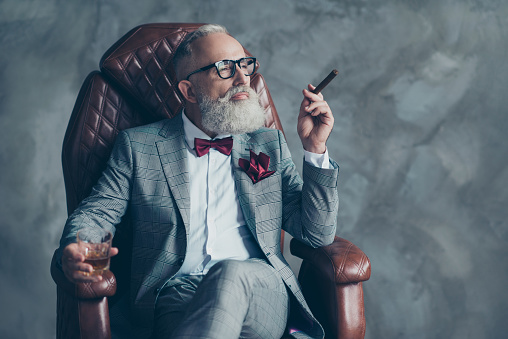 Retrato de elegante elegante elegante viril ensueño moda soñando arreglado a millonario jefe brutal empresa grande sentado en cuero sillón fumar cigarrillo beber bebida aislado sobre fondo gris photo