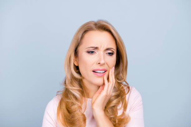 retrato de hermosa, joven, mujer que sufre de dolor de terribles dientes fuertes, tocando la mejilla con la mano sobre fondo gris, dolor dental, odontología, odontólogos, concepto de salud - beauty beautiful tired blond hair fotografías e imágenes de stock