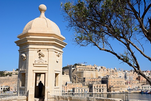 Man looking at the view towards Valletta from a bastion in the Gardjola Gardens with people enjoying the setting, Senglea, Malta, Europe.