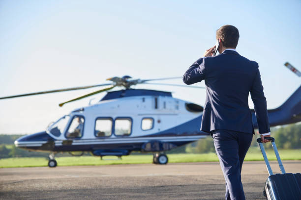 携帯電話で話をしながら、ヘリコプターに向かって歩くビジネスマンの背面図 - ヘリコプター ストックフォトと画像