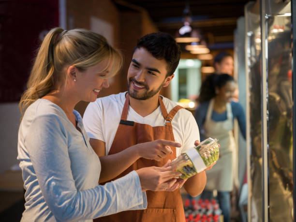 istock Cheerful salesman suggesting a new salad to a beautiful customer both smiling 931275786