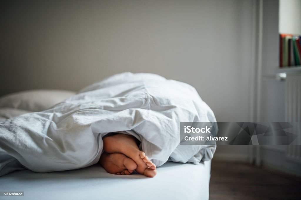 Low section of young woman sleeping in bed Low section of young woman sleeping in bed. Female's bare feet under blanket in bedroom. She is resting at home. Sleeping Stock Photo