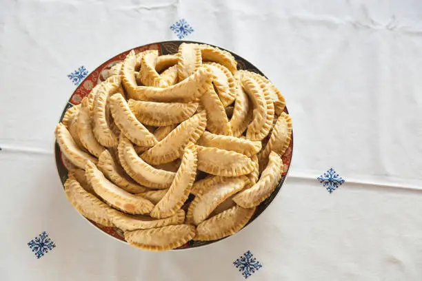 Plate of fresh baked Kaab El Ghazal, a moroccan sweet also known as gazzele horns due to his peculiar shape made mainly with almonds and wheat flour. Shot on a traditional handmade tablecloth