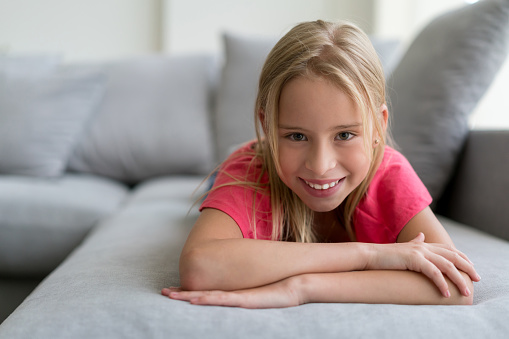 Portrait of little girl relaxing on the couch at home looking at camera very happy and smiling