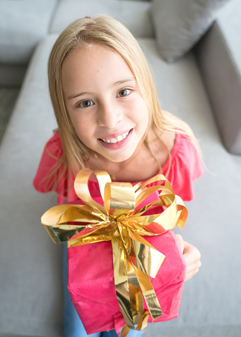 Close up of beautiful latin american girl holding a present on her lap looking at camera very happy and smiling