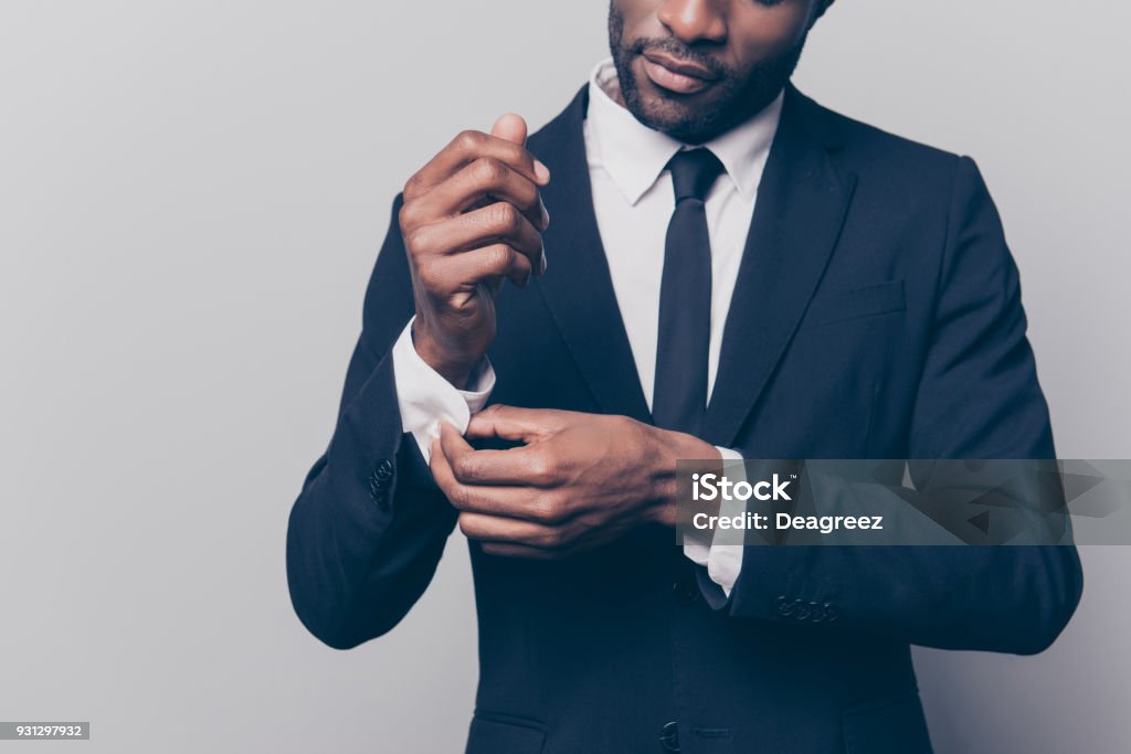 Cropped half face portrait of trendy, attractive, stunning man in black tuxedo with tie fasten button on sleeve cuffs of his white shirt, isolated on grey background Men Stock Photo