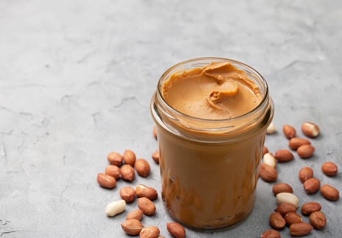 peanut butter in a glass jar, peanuts on a gray concrete background.