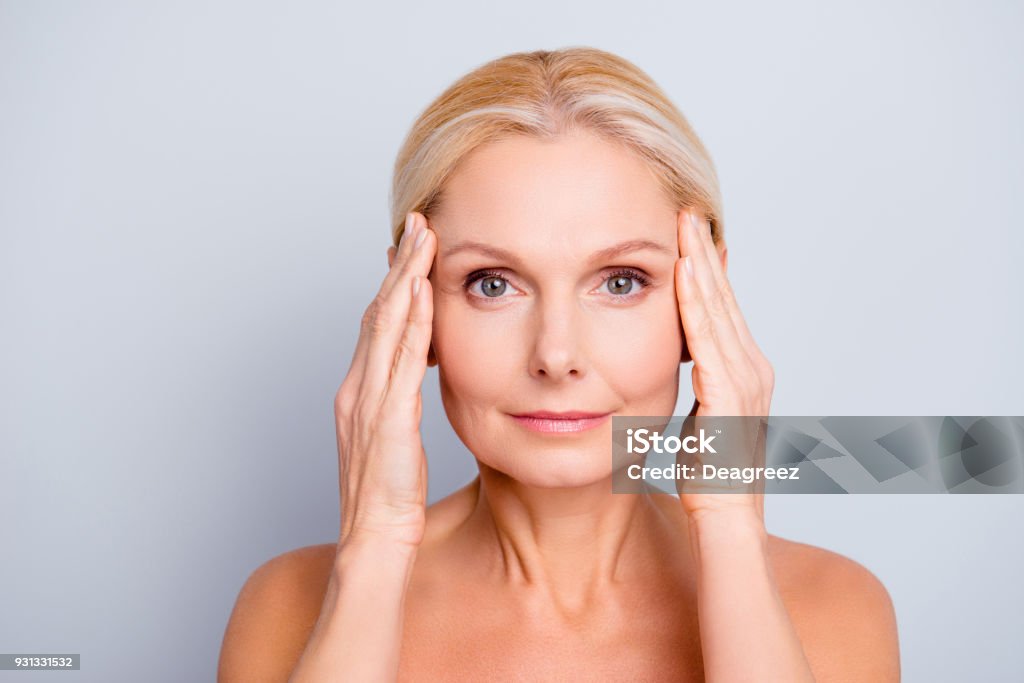 Portrait of pretty, attractive, charming, naked, nude woman touching temples with hands, isolated on grey background,  after peeling, lotion, mask, perfection, wellness, wellbeing, hydration concept Human Face Stock Photo