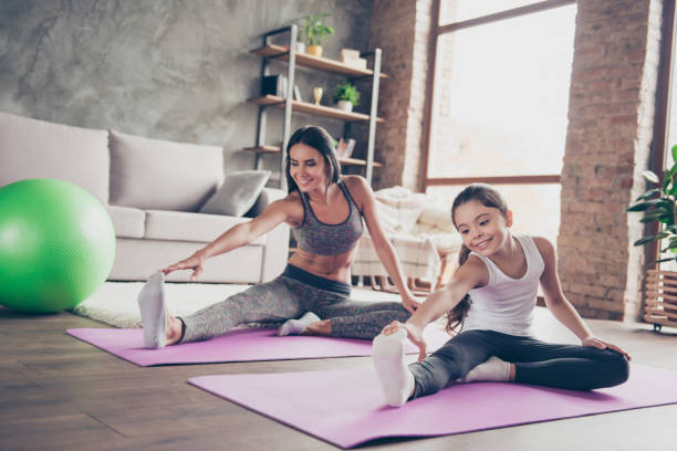 we love fun sport! charming sportive slim active energetic beautiful mum and cute lovely adorable careless daughter wearing sport-clothes sitting on the floor touching toes on the outstretched legs - the splits ethnic women exercising imagens e fotografias de stock